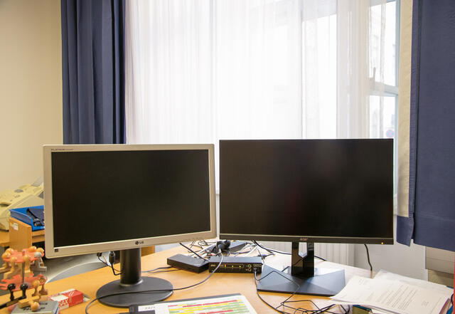 Dieses Beispiel zeigt eine arbeitsmedizinisch suboptimale Arbeitsplatzgestaltung, da sich direkt hinter den Bildschirmen ein Fenster befindet. Dadurch sind die Augen ständig dem Gegenlicht ausgesetzt, was sich langfristig negativ auswirkt. Besser wäre es, die Bildschirme seitlich zum Fenster auszurichten. (Foto: RedTD/Selina Lukas)